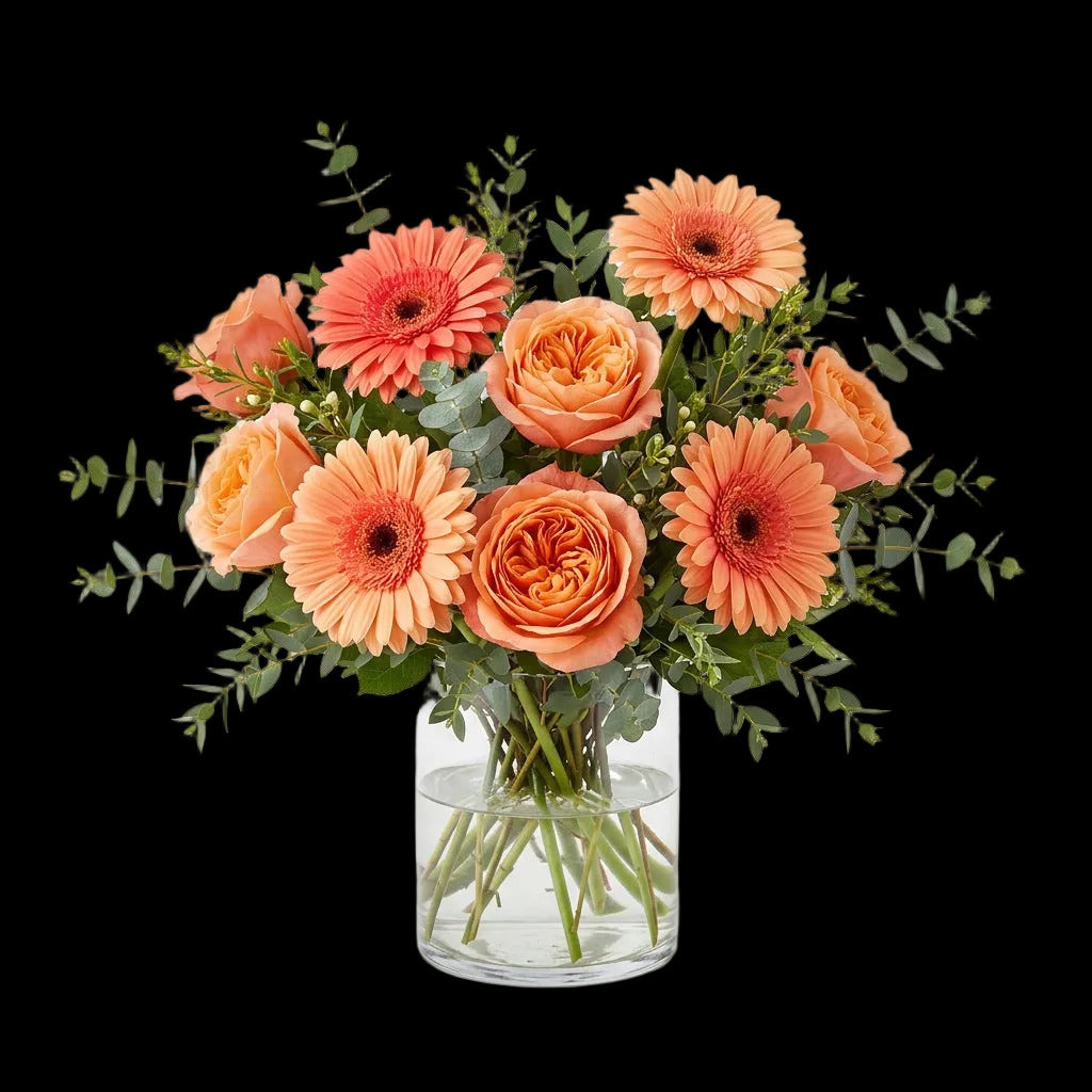 The Miami Birthday Standard arrangement with peach and coral roses, gerbera daisies and greenery in a clear glass vase.