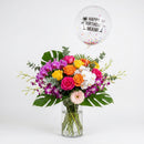 Fiesta & Blooms arrangement with colorful roses, purple and white orchids, tropical leaves and a Happy Birthday Miami balloon.