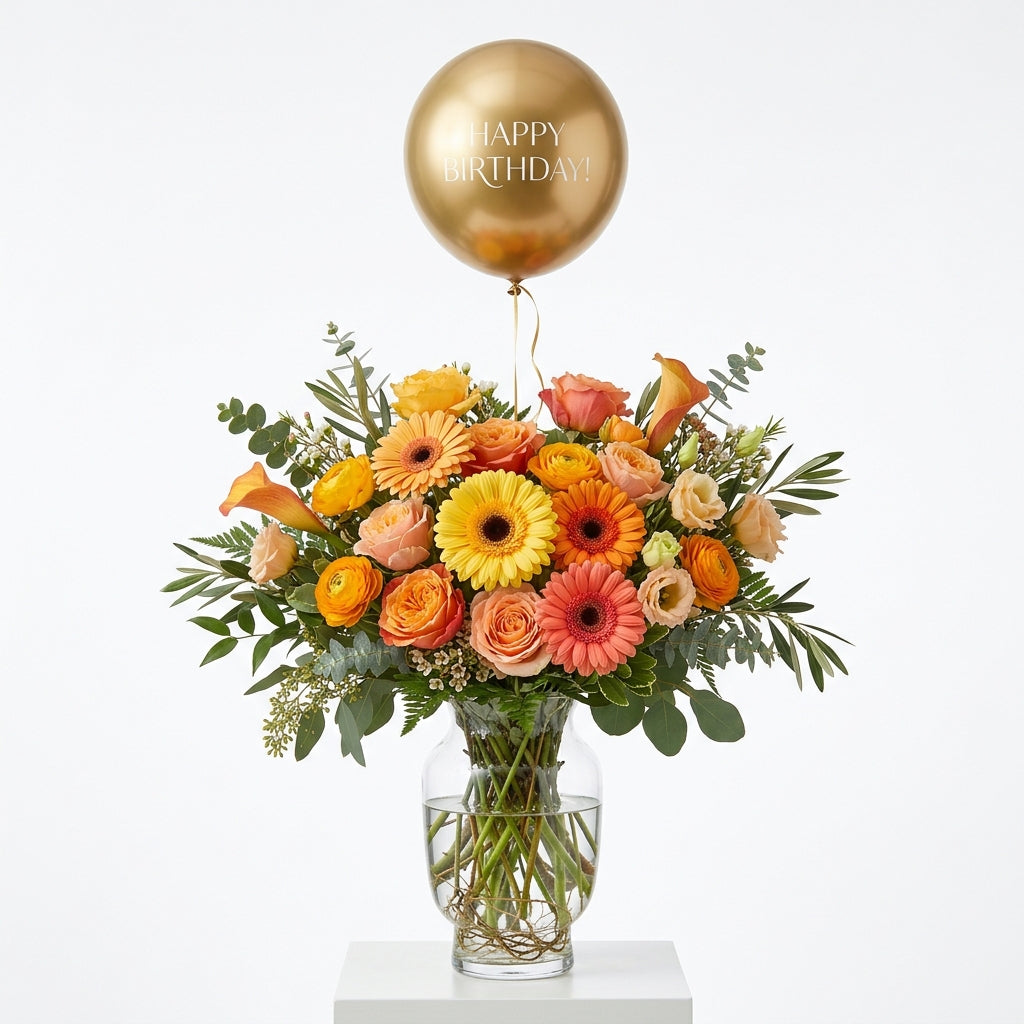 Golden Birthday Glow yellow, orange and peach floral arrangement in a glass vase with a gold Happy Birthday balloon.