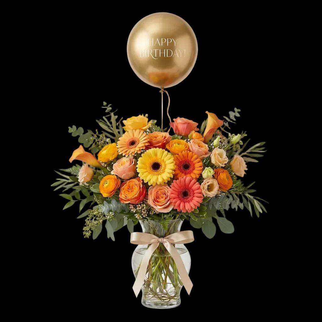 Golden Birthday Glow yellow, orange and peach floral arrangement in a glass vase with a gold Happy Birthday balloon.