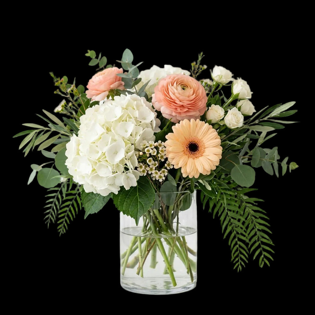 Radiant Celebration Bouquet with white hydrangea, soft peach flowers and layered greenery in a clear glass vase.