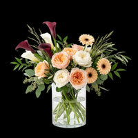 Tropical Birthday Chic arrangement with peach and cream roses, burgundy calla lilies and peach gerbera daisies in a glass vase.