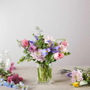 Colorful spring flower bouquet with tulips and irises in a clear vase on a table.