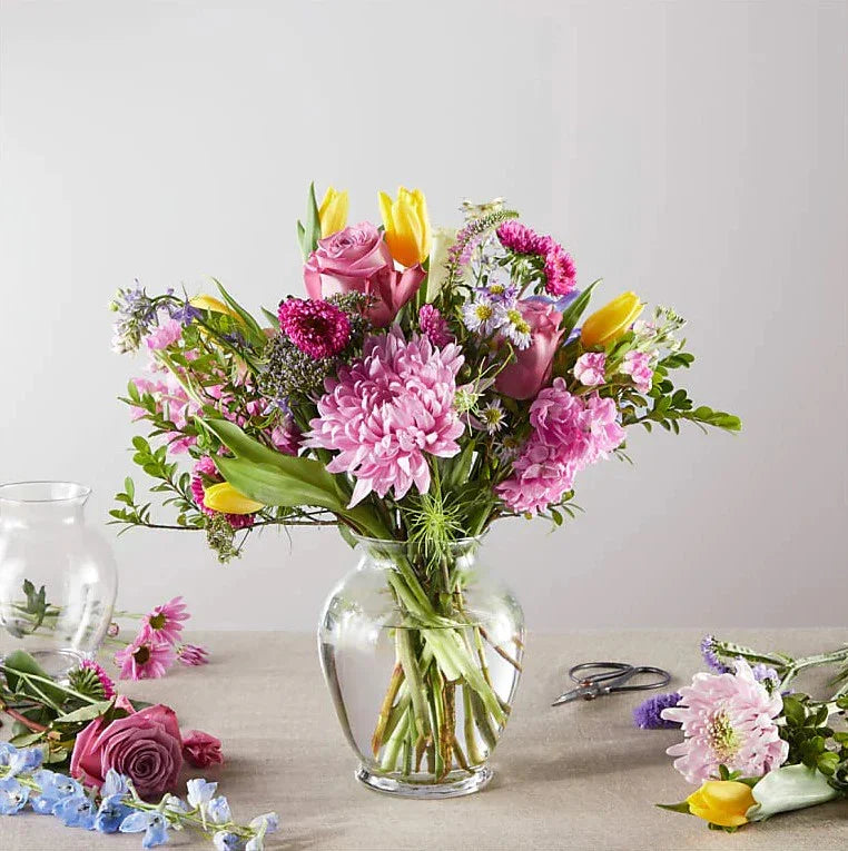 Spring flower bouquet with pink roses, yellow tulips, and mixed blooms in a glass vase