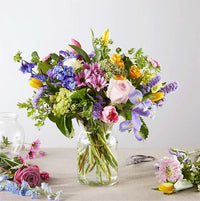 Colorful spring flower bouquet in glass vase with roses, tulips, and daisies for delivery