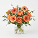 The Miami Birthday Standard arrangement with peach and coral roses, gerbera daisies and greenery in a clear glass vase.
