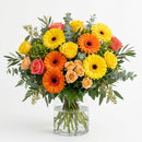 Miami Sunshine Birthday arrangement with yellow and orange gerbera daisies, roses and greenery in a clear glass vase.