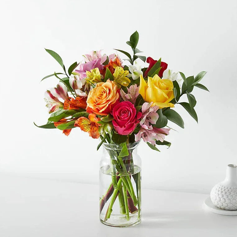 Bright mixed flower bouquet with roses and lilies in a glass vase for flower delivery